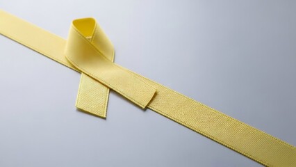 Symbol of hope and awareness: a textured yellow awareness ribbon displayed diagonally on a subtle gray background