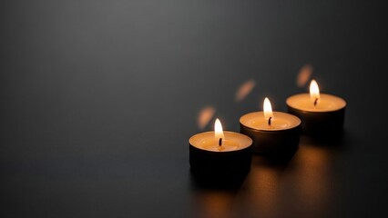 Three small tea light candles with warm glowing flames illuminating a dark, reflective surface, creating a serene and somber atmosphere.