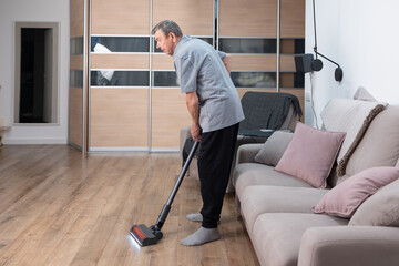 Elderly man vacuuming floor at home