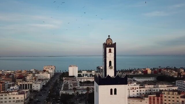 Cinematic drone shot orbiting a traditional mosque minaret during golden hour, with long shadows and the Mediterranean Sea in the background.