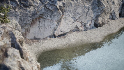 A stunning view showcases a rocky coastline, where clear water meets a pebbled beach. The scene captures the serene beauty of nature during the golden hour of sunset.