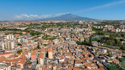 Obraz premium Aerial view at morning of the city of Catania, Sicily, southern Italy. In the background, on the horizon, Mount Etna looms in silhouette, dominating the panorama. It is a sunny summer day.