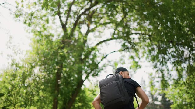 Young Man Springs Energetically Among Trees, Individual With Backpack Energetically Soaring Through Sunlit Forest, Man With Enthusiastic Expression Leaps Through Brightly Lit Summer Park Trees