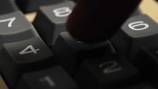 Close up of fingers pressing number keys on a vintage calculator while entering calculations