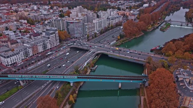 Aerial drone view of a metro train crossing a bridge over the Marne River near Paris. Views of the busy highway traffic, Saint-Maurice lock, and autumn trees. Ideal for transport and city concepts