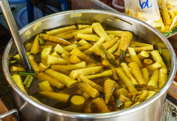 Pickled yellow bamboo shoots in brine soup inside large metal pot at Thai fresh market. Traditional Asian fermented vegetable ingredient for sour curry cooking and local street food stall cuisine.