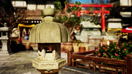 A charming stone lantern stands prominently in a tranquil Japanese garden, surrounded by lush greenery and vibrant flowers as sunlight bathes the scene, creating a peaceful atmosphere.