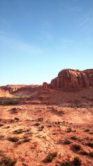 A vast desert scene features stunning red rock formations and a bright blue sky. The sun illuminates the rugged terrain, showcasing the natural beauty of the arid environment.