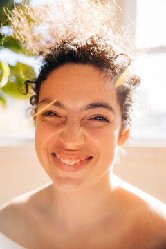 Smiling woman squints in bright golden sunlight indoors