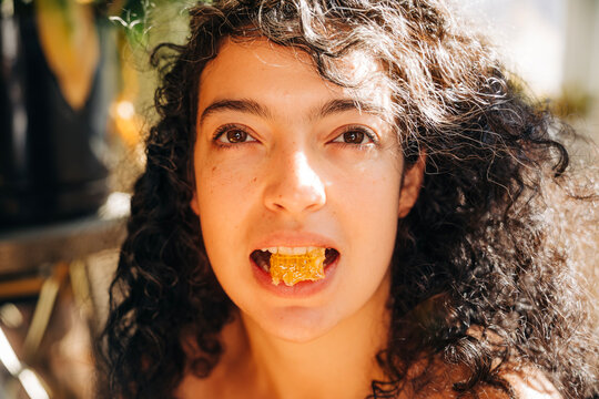 Young woman eating natural honeycomb looking at camera