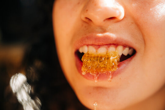 Person biting into honeycomb with honey dripping from mouth