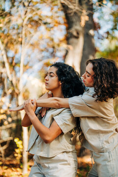 Two women pose with intertwined arms in autumn forest