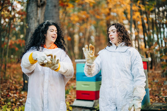 Two beekeepers in suits talk and laugh in autumn forest apiary