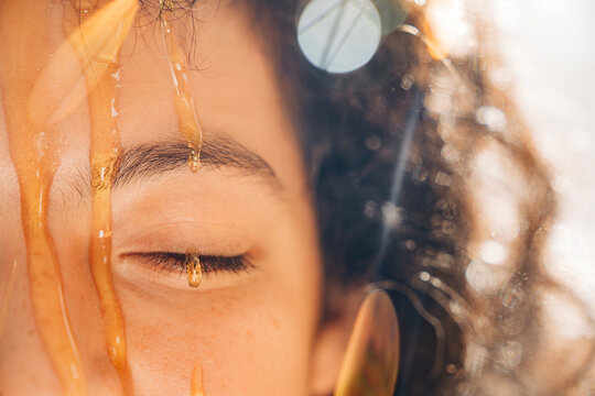 Woman's closed eye with honey dripping on face