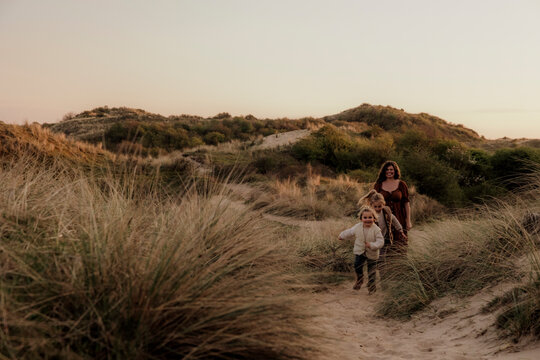 Woman and two children walking through grassy coastal dunes