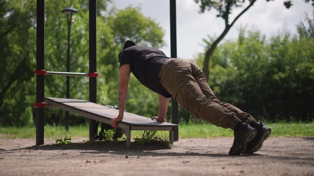 Bench Incline PushUp By White Man, Focused Chest And Triceps Engagement On Public Bench, LowAngle Sunlight, Khaki Trousers, Steady Controlled Reps For UpperBody Strength And Core Stability
