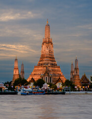 Fototapeta premium Wat Arun temple shines at sunset on the Chao Phraya River in Bangkok, Thailand