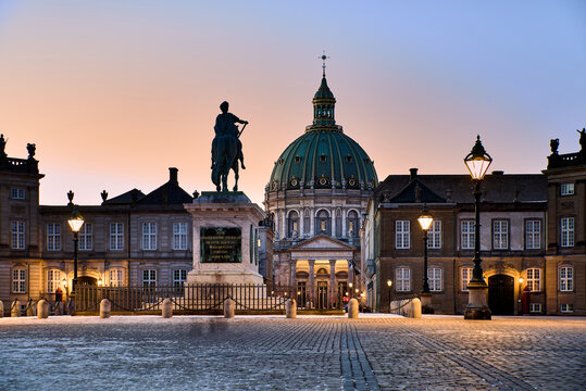 Sunset over Amalienborg Palace Square with Frederik 's Church dome and equestrian statue glowing above cobblestones and lamplit facades, expressing Copenhagen 's royal charm and high quality of life