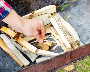 Hand lighting kindling with fire starter cubes in a barbecue grill