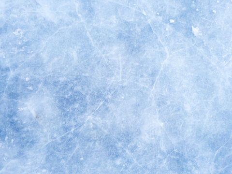 A background of blue ice with scratches and cracks. The frozen surface of a lake, a Christmas winter skating rink. A textured backdrop for New Year's, winter sports, and entertainment.