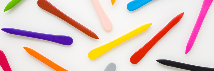 Pattern of colorful wax crayons on white table background. Wide banner. Closeup. Top down view.