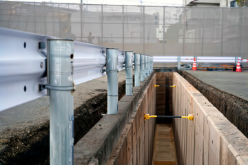 Deep utility trench reinforced with hydraulic shoring struts and metal guardrails.