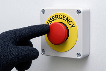 Gloved hand presses red emergency stop button on white industrial panel.