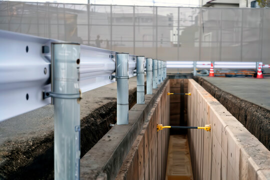 Deep utility trench reinforced with hydraulic shoring struts and metal guardrails.