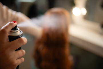 Hairstylist spraying hair with aerosol can in salon