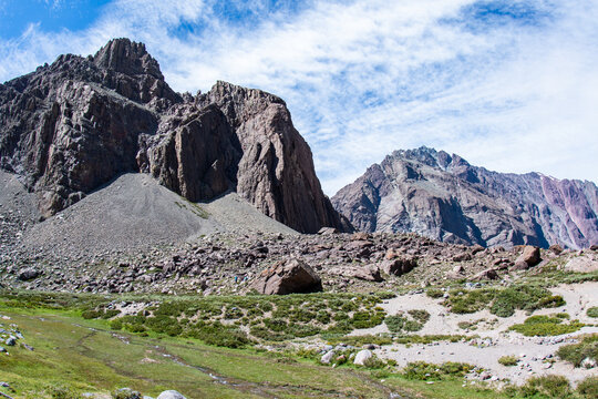 View of jagged peaks rise in stark contrast to the green valley below, under a sky streaked with wispy clouds, San Jos&eacute; de Maipo, Santiago Metropolitan Region, Chile.