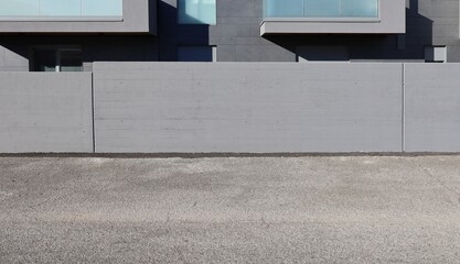 Gray painted concrete fence in front of a gray stone tiled modern building, at roadside. Street in front. Background for copy space.