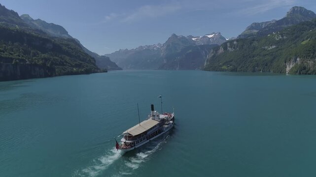 Aerial view of a boat sailing on the turquoise waters of Lake Lucerne, framed by majestic mountains and lush green forests, Ingenbohl, Schwyz, Switzerland.