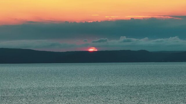 Aerial view of the sun setting over calm waters meeting a distant dark horizon under a sky painted with hues of orange and blue, Cres, Primorsko-goranska zupanija, Croatia.