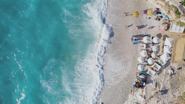 Aerial view of turquoise water meeting the shore where beach umbrellas sit on the sand, a scenic contrast of colors, Ksamil, Qarku i Vlores, Albania.