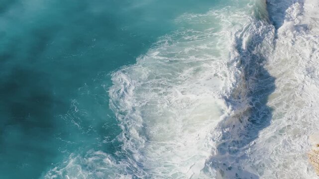 Aerial view of turquoise waters churn into foamy white waves as they crash against the pale, rocky shore, creating a dynamic contrast, Ksamil, Qarku i Vlores, Albania.