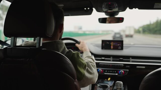 Rear view of a man driving a modern car on the highway, focusing on road safety. Navigation technology, travel insurance during a road trip, and car insurance.