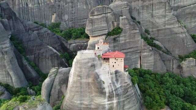 Aerial view of the Monastery of Rousanou perched atop a towering rock formation amidst lush greenery, Kalabaka, Trikala, Greece.