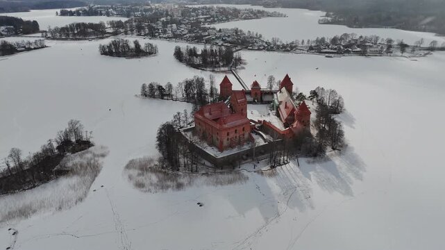Aerial view of Trakai Island Castle standing proudly amid the frozen lake, a striking contrast against the snowy landscape, Trakai, Lithuania.
