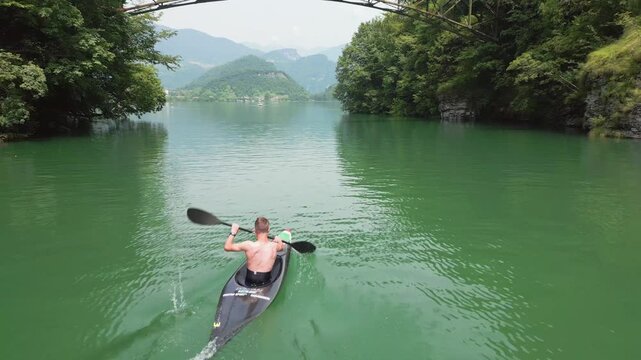 A man in a canoe paddling on a lake surrounded by nature. Aerial view of a canoeist practicing canoeing, a healthy outdoor activity