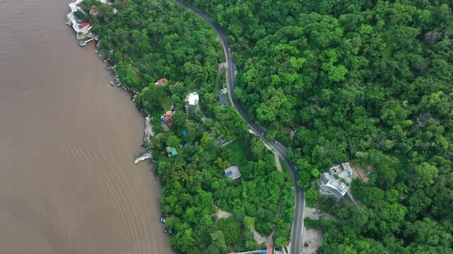 Aerial view of the rugged coastline meeting the dense, verdant forest, with houses nestled among the trees and a winding road cutting through, Boca de Tomatlan, Jalisco, Mexico.