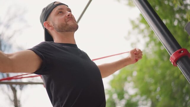 Man Exercises Outdoors, Person Practicing Resistance Training For Chest In Open Park Setting, Individual Doing Resistance Band Chest Exercise In Park With Attentive Focus And Regular Breathing