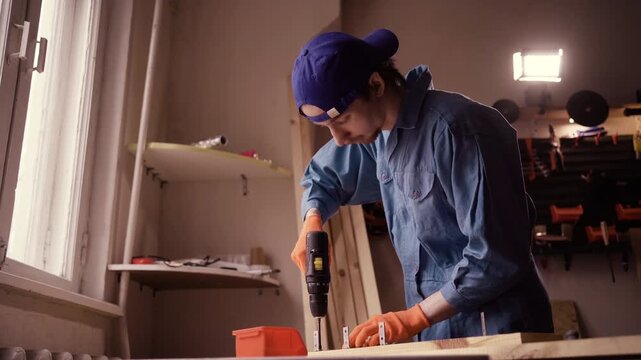 Professional handyman in overalls drilling a hole in wooden plank using electric power drill
