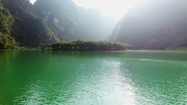 A drone flies over the Trang an Valley, a large body of water, with mountains covered in dense forest to the right and left.