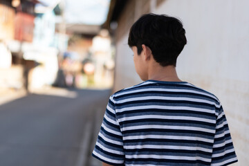 A teenage boy wearing a zebra-print t-shirt stands and walks alone in the street, looking isolated and lonely.