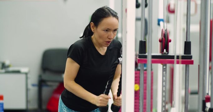 Gym workout. Triceps exercise. Middle aged Caucasian woman trains hers triceps muscles in the gym. Focused triceps workout by a woman building arm strength in the gym.