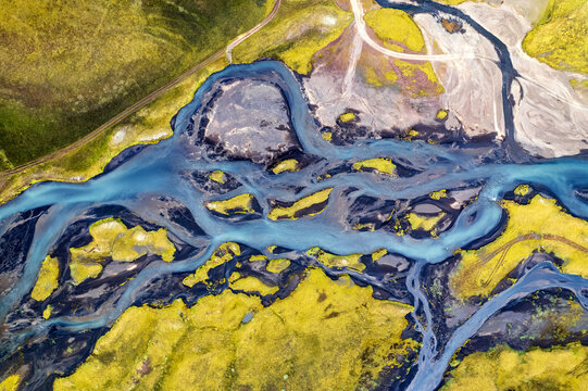 Aerial view of glacial river carves through vibrant green and yellow moss-covered landscape near Holmsarfossar, Skaftarhreppur, Iceland.