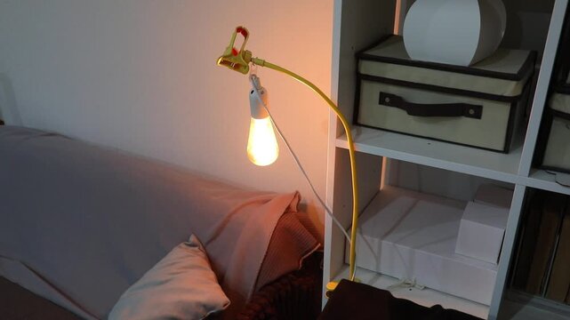 Cozy home interior with a retro smart light lamp clipped to a shelf, providing warm illumination next to a sofa and decorative boxes.