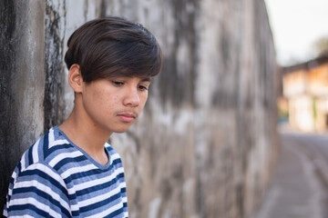 A teenage boy wearing a zebra-print t-shirt stands sadly and quietly by a gray wall.
