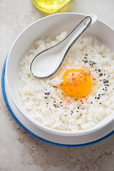 Bowl of tamago kake gohan or japanese warm rice mixed with a raw chicken egg, vertical shot on a beige stone surface, middle closeup