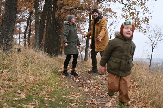 A mother, father, and son take a nature walk in a national park, warmly dressed, in the fall or winter without snow. Warm clothing for a hike for the whole family. Types of winter recreation - Powered by Adobe